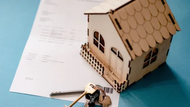 Modellino di casa in legno con chiavi su un contratto di mutuo